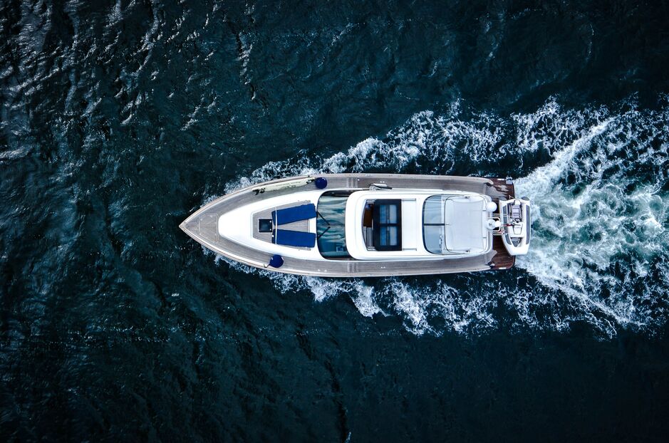 Top view of a motorized boat sailing through water leaving a foamy trail